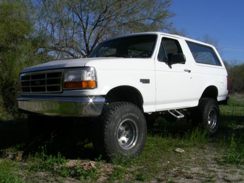 1996 Ford Bronco - This lifted white Ford Bronco is shown from a three-quarter front angle, parked outdoors on a sunny day.