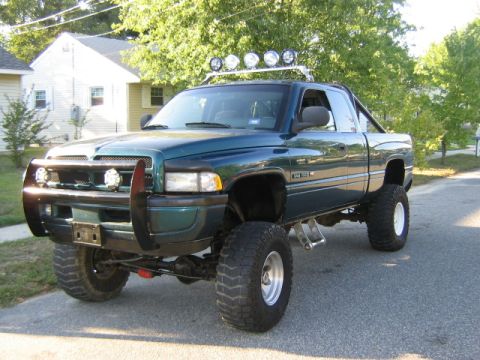 1998 Dodge 1500 - A lifted green 1998 Dodge 1500 pickup truck is parked on a residential street, modified for off-road use.