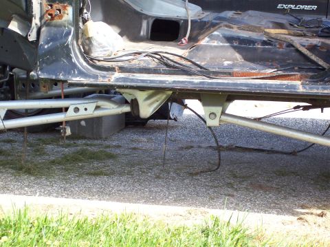 1990 Ford Bronco - The underside of a heavily damaged vehicle chassis is visible, showing exposed metal and wiring.