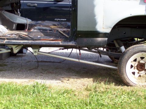 1990 Ford Bronco - Side view of a heavily modified truck chassis, with a dark Ford Explorer visible in the background.