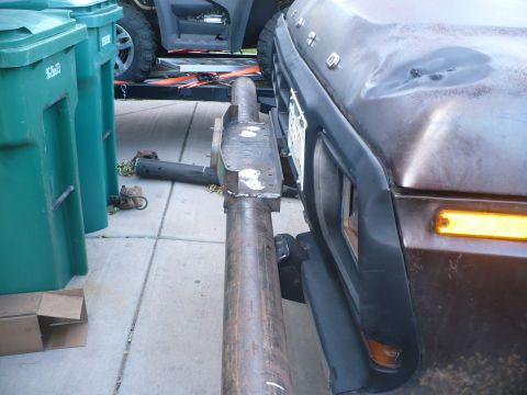 1979 Ford Bronco - A custom bumper extension is attached to the front of a brown 1979 Ford Bronco, with trash cans and another vehicle visible in the backgrou…