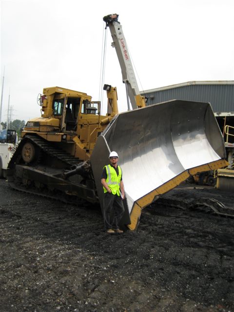 1990 Ford Bronco - A man stands beside a large yellow bulldozer, dwarfed by its immense blade.