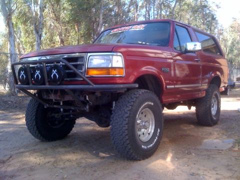1989 Ford Bronco - This red Ford Bronco features a custom front bumper and auxiliary lights, suggesting off-road modifications.