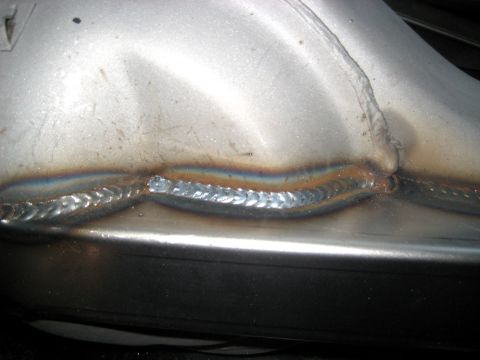 1996 Ford Bronco - Close-up view of a welded metal exhaust pipe, showing detailed weld seams and heat discoloration.
