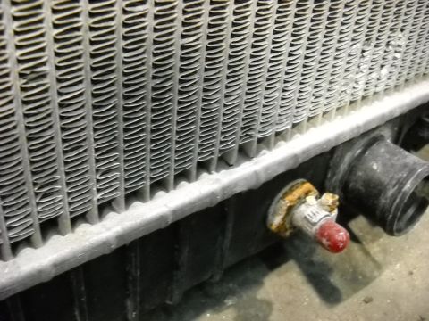 1986 Ford C-350 (Centurion Conversions) - Close-up of a vehicle radiator, showing its fins and a drain plug with corrosion.