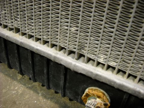 1986 Ford C-350 (Centurion Conversions) - Close-up view of a vehicle radiator, showing the fins and a corroded fitting at the bottom.