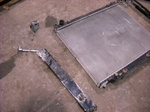1986 Ford C-350 (Centurion Conversions) - A radiator and a metal support beam lie on a concrete floor, possibly after removal for repair.