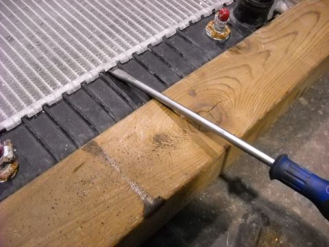 1986 Ford C-350 (Centurion Conversions) - Close-up of a radiator being worked on with a screwdriver and wood.