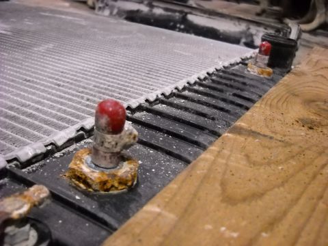 1986 Ford C-350 (Centurion Conversions) - This close-up shows a radiator component with visible rust on its mounting hardware and a wooden surface nearby.