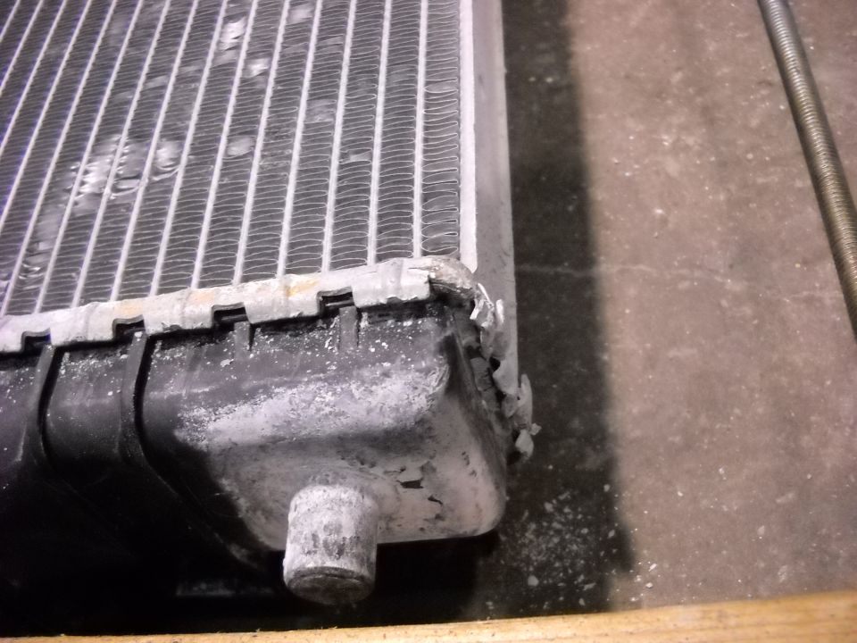 Close-up of a damaged vehicle radiator with bent fins and a cracked plastic tank