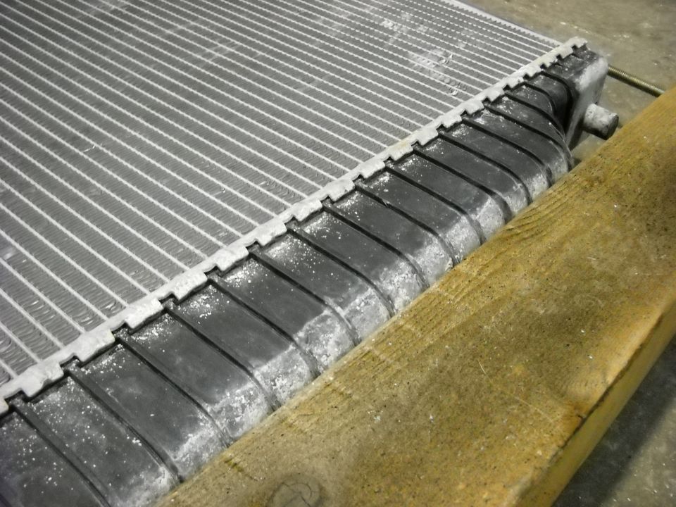 Radiator with corroded fins and black plastic side tanks, resting on wood