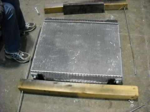 1986 Ford C-350 (Centurion Conversions) - A radiator is shown on a concrete floor, supported by wooden blocks and surrounded by metal rods, suggesting repair or replacement.