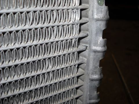 1986 Ford C-350 (Centurion Conversions) - Close-up view of a damaged radiator core, showing bent fins and a section of the metal frame.