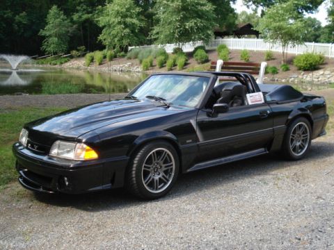 2000 Ford Excursion - A black convertible Mustang is parked on a gravel surface near a body of water with a fountain.