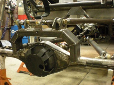 Suzuki Samurai - Bare-metal axle housing under construction on jack stands in a fab shop, fitted with a black nodular differential cover and a fabricated tr…