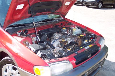 2001 Ford Crown Victoria - Engine bay of a red Subaru Outback Sport. Another Subaru Outback Sport is parked behind it.