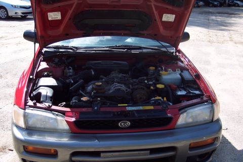 2001 Ford Crown Victoria - The engine bay of a red Subaru Impreza Outback Sport is visible with the hood raised, and another vehicle is parked in the background.