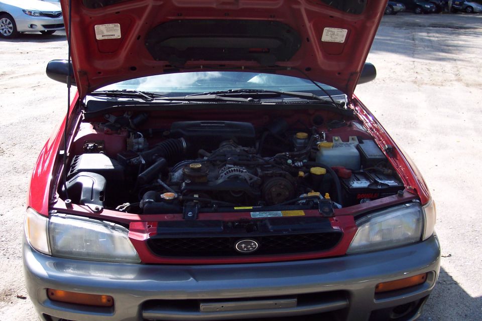 Red Subaru Impreza Outback Sport with hood open showing the engine bay. Another white Subaru is parked nearby