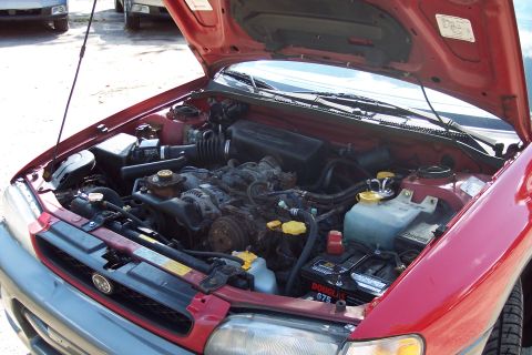 2001 Ford Crown Victoria - The engine bay of a red Subaru is visible with the hood open, revealing the engine and surrounding components.