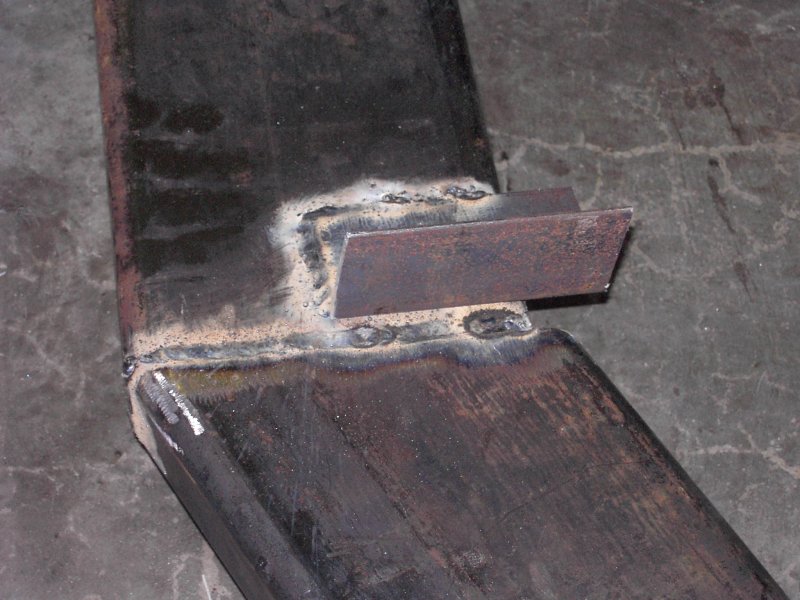 Steel bracket tab welded to a bent rectangular steel bar, fresh welds visible, on a concrete floor