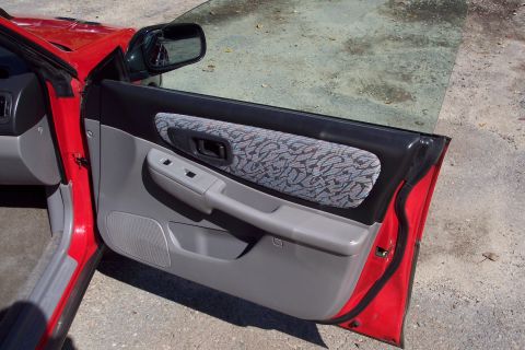 2001 Ford Crown Victoria - The interior door panel of a red vehicle features a gray finish with a patterned fabric insert and a prominent door handle.