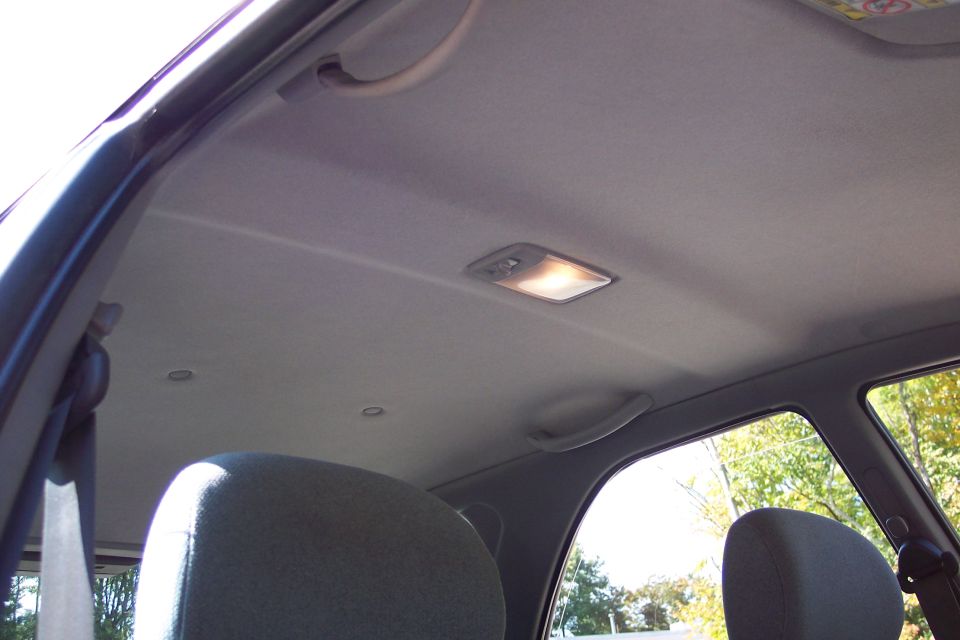 Car interior showing grey headliner, dome light, and grab handles. Seats are visible