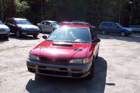 2001 Ford Crown Victoria - Red Subaru Impreza WRX parked in a lot with other cars and trees in the background.