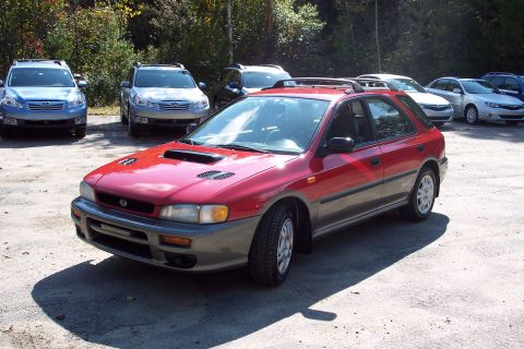 2001 Ford Crown Victoria - A red Subaru Impreza wagon is parked in a lot with several other vehicles visible in the background.