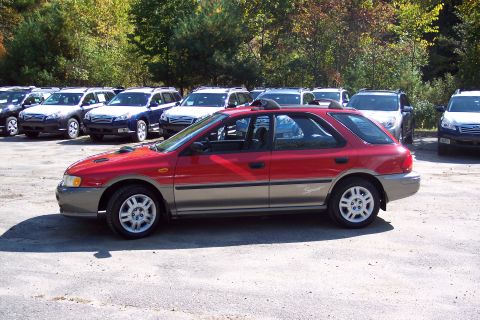 2001 Ford Crown Victoria - A red and tan Subaru Impreza Outback Sport wagon is parked in a lot with other vehicles visible in the background.