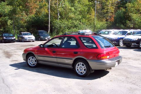 2001 Ford Crown Victoria - This red and grey Subaru Outback Sport wagon is seen from the rear 3/4 angle with other vehicles parked in the background.