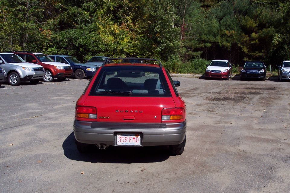 Red Subaru Outback hatchback parked in a lot, rear view. Other cars are visible in the background