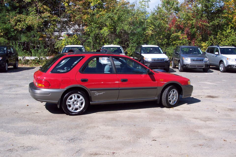Red and gray Subaru Impreza Outback Sport wagon, side view. Other SUVs parked behind