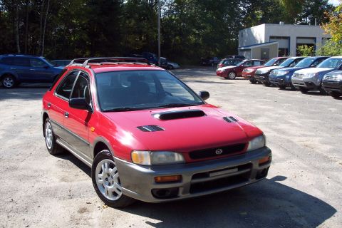 2001 Ford Crown Victoria - A red 1998 Subaru Impreza Outback Sport is parked in a lot with other vehicles and a building in the background.