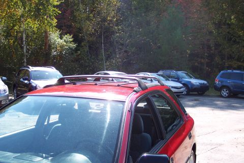 2001 Ford Crown Victoria - A red Subaru Outback Sport is parked in a lot with other vehicles and trees in the background.