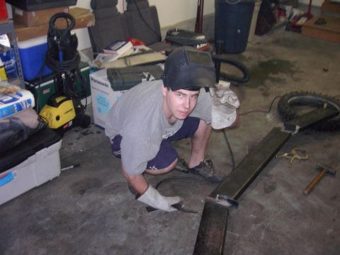1980 Ford Bronco - A person in a welding mask crouches down to work on a metal structure in a cluttered garage.