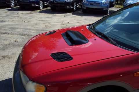 2001 Ford Crown Victoria - Close-up of the hood of a red Subaru Impreza Outback Sport, a prominent black scoop and ventilation grilles, with other vehicles visible in…
