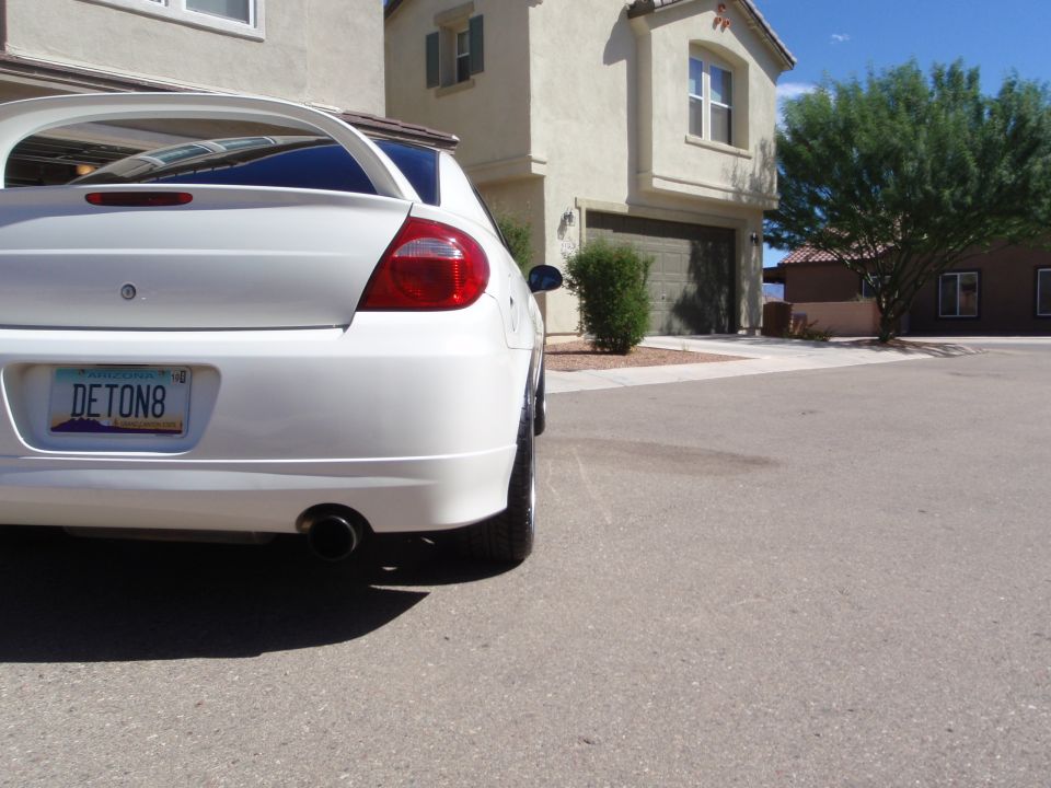Rear view of a white sedan with a spoiler and custom license plate 'DETON8'