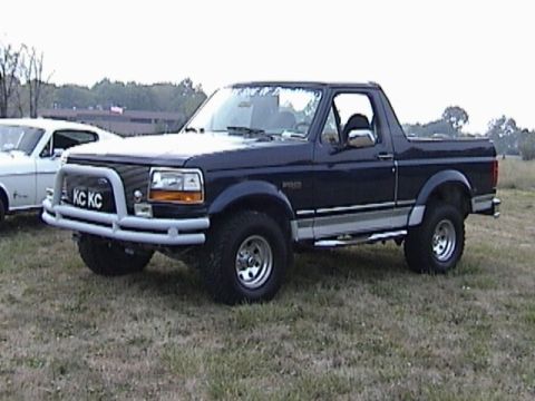 1995 Ford Bronco - A dark blue Ford Bronco is parked on a grassy field next to a white car.