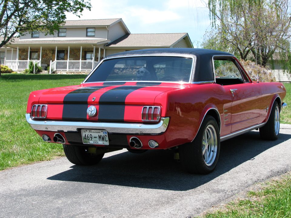 1966 Ford Mustang coupe, red with black stripes, rear driver's side view, parked on driveway.