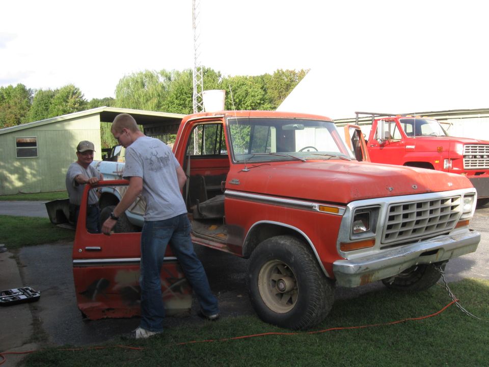 Two men working on the door of a red Ford pickup truck.
