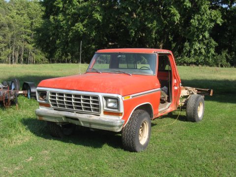 1979 Ford F-100 - This orange 1979 Ford F-100 pickup truck is parked outside with the driver's door removed.