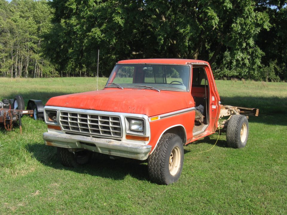 Orange 1979 Ford F-100 pickup truck, driver's door removed, parked on grass