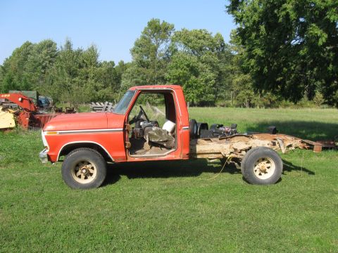 1979 Ford F-100 - This orange Ford F-Series truck from 1973 is missing its bed and has its passenger door ajar.