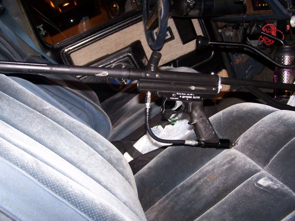 Paintball gun resting on the velour seats inside a vehicle. Text on gun reads 'SPIDER ELITE'