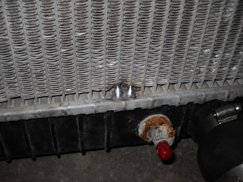 1986 Ford C-350 (Centurion Conversions) - Close-up of a damaged vehicle radiator, highlighting bent fins and a corroded drain valve.