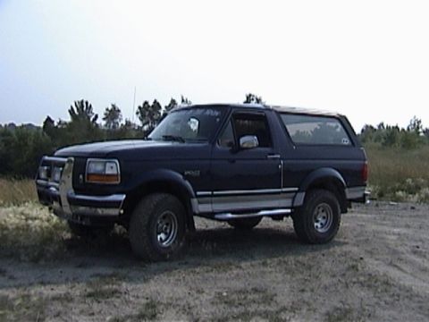 1995 Ford Bronco - A dark blue Ford Bronco is parked on a dirt lot with a brush guard on its front bumper.