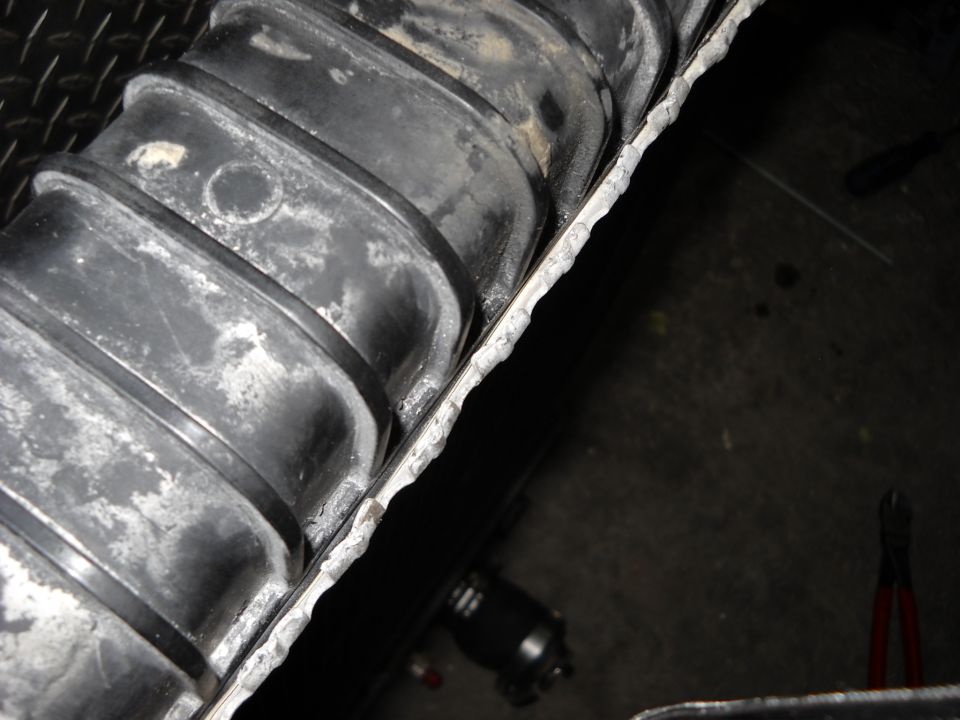 Close-up of a ribbed black radiator hose with white residue, pressed against a corrugated metal edge