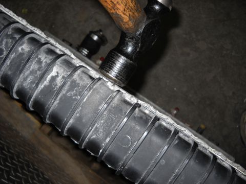 1986 Ford C-350 (Centurion Conversions) - A hammer is used to strike the plastic tank of a car radiator, likely for repair or removal.