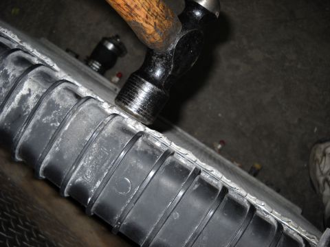 1986 Ford C-350 (Centurion Conversions) - A hammer impacts a vehicle radiator, suggesting repair or damage.