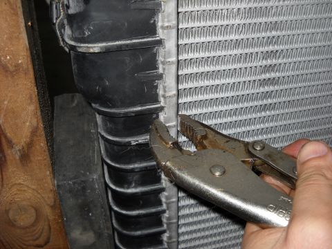 1986 Ford C-350 (Centurion Conversions) - Pliers gripping a radiator hose connection next to the radiator fins.
